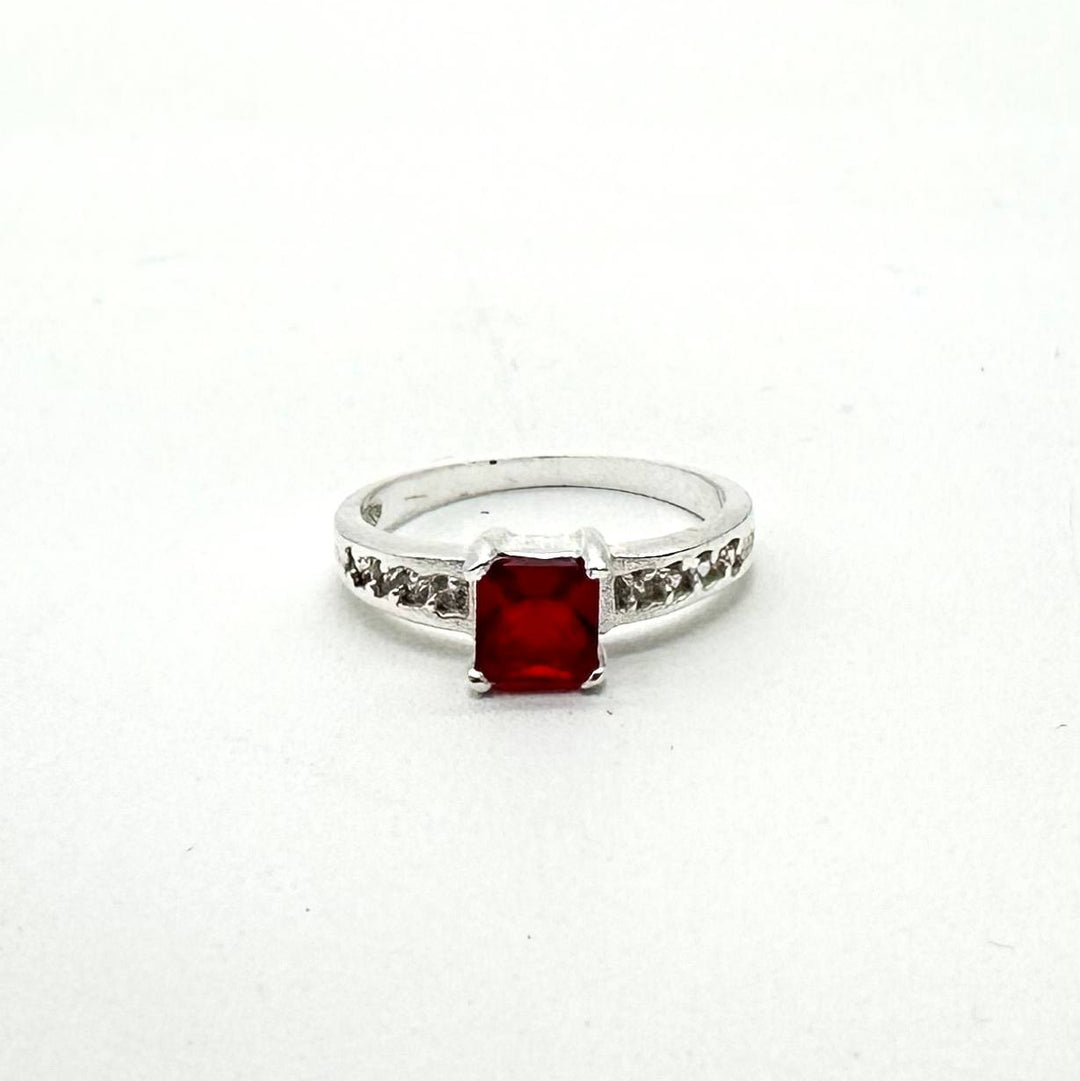 Anillo de plata 925 con cristal rojo corte esmeralda y zirconias laterales brillantes.