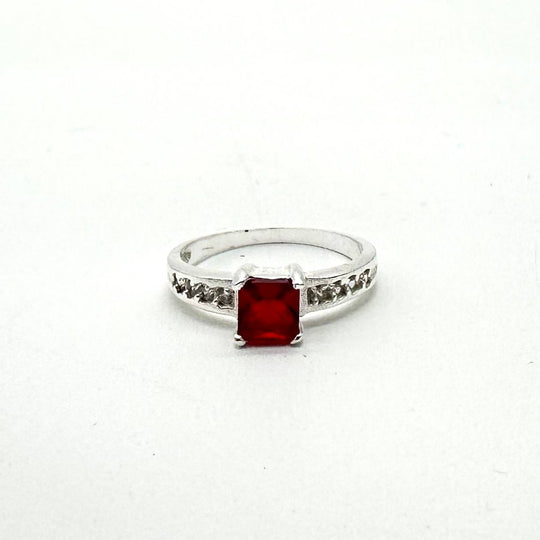 Anillo de plata 925 con cristal rojo corte esmeralda y zirconias laterales brillantes.
